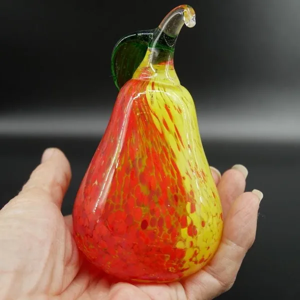 Kosta Boda pear clutched in hand, showing saturated red side, leaf arrangement, and three-dimensional form clarity