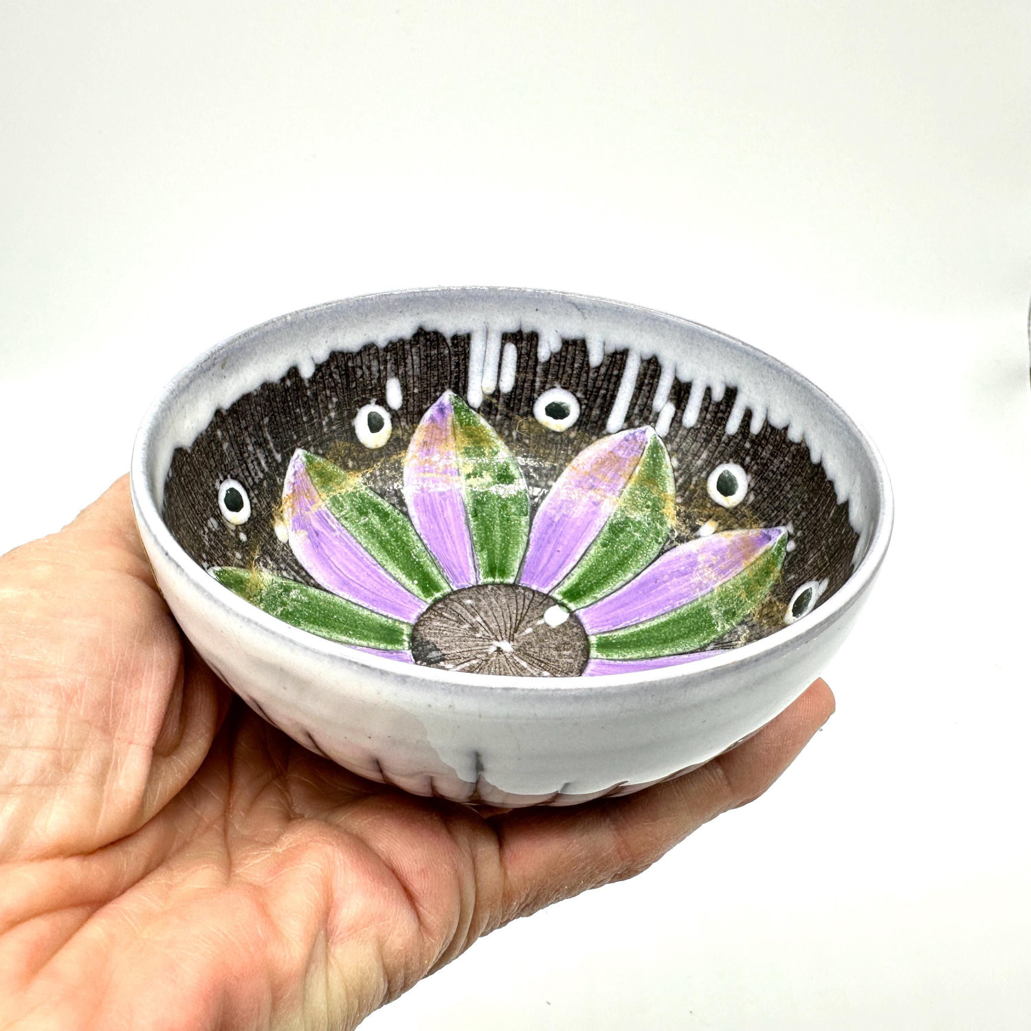 Laholm Keramik Swedish pottery bowl held in hand, purple and green flower design on dark interior, white drip-glaze exterior