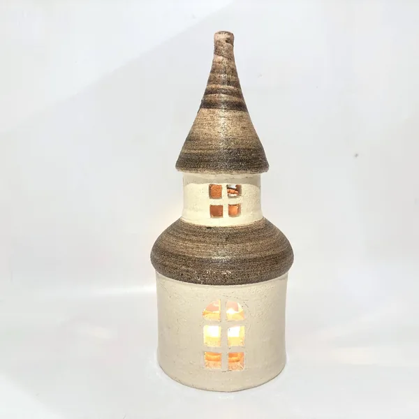 Lit ceramic candle house with warm golden light glowing through all window openings, rounded base, complete architectural for