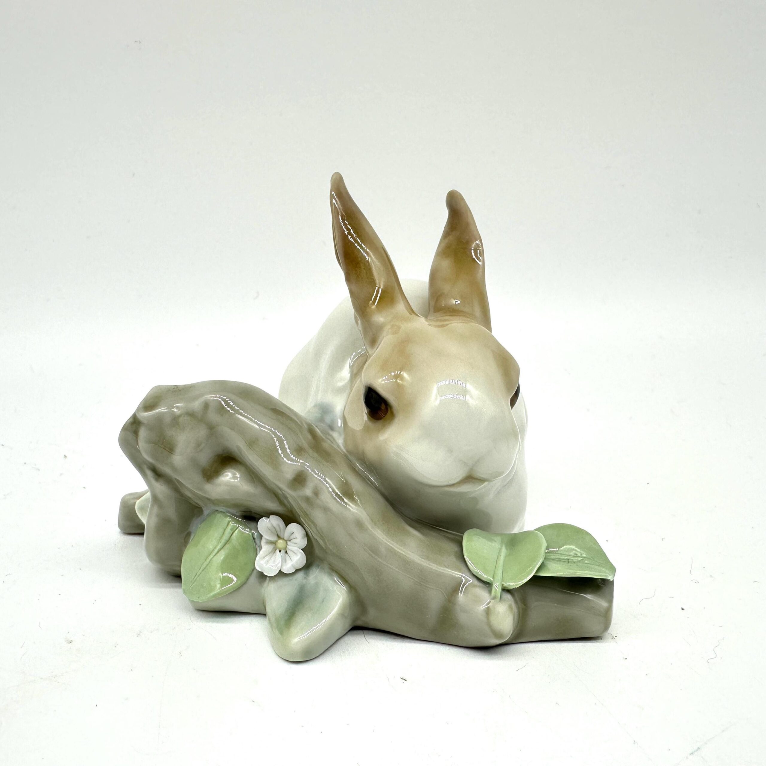 Lladro porcelain bunny figurine shot from three-quarter angle showing cream body, tan ears, and decorative leafy base with wh