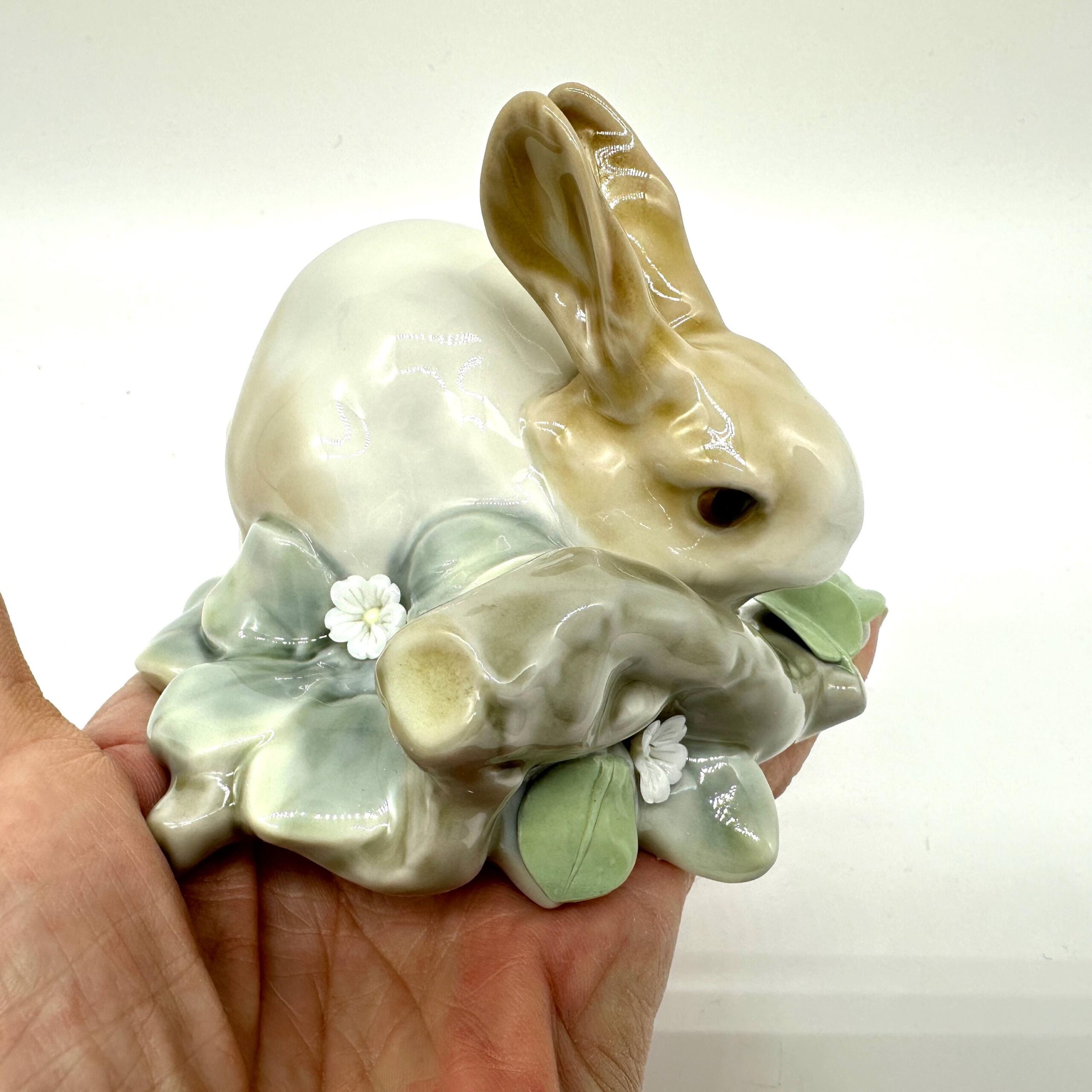 Lladro porcelain rabbit figurine in hands showing seated posture, brown ear details, cream glaze, and sculpted green botanica