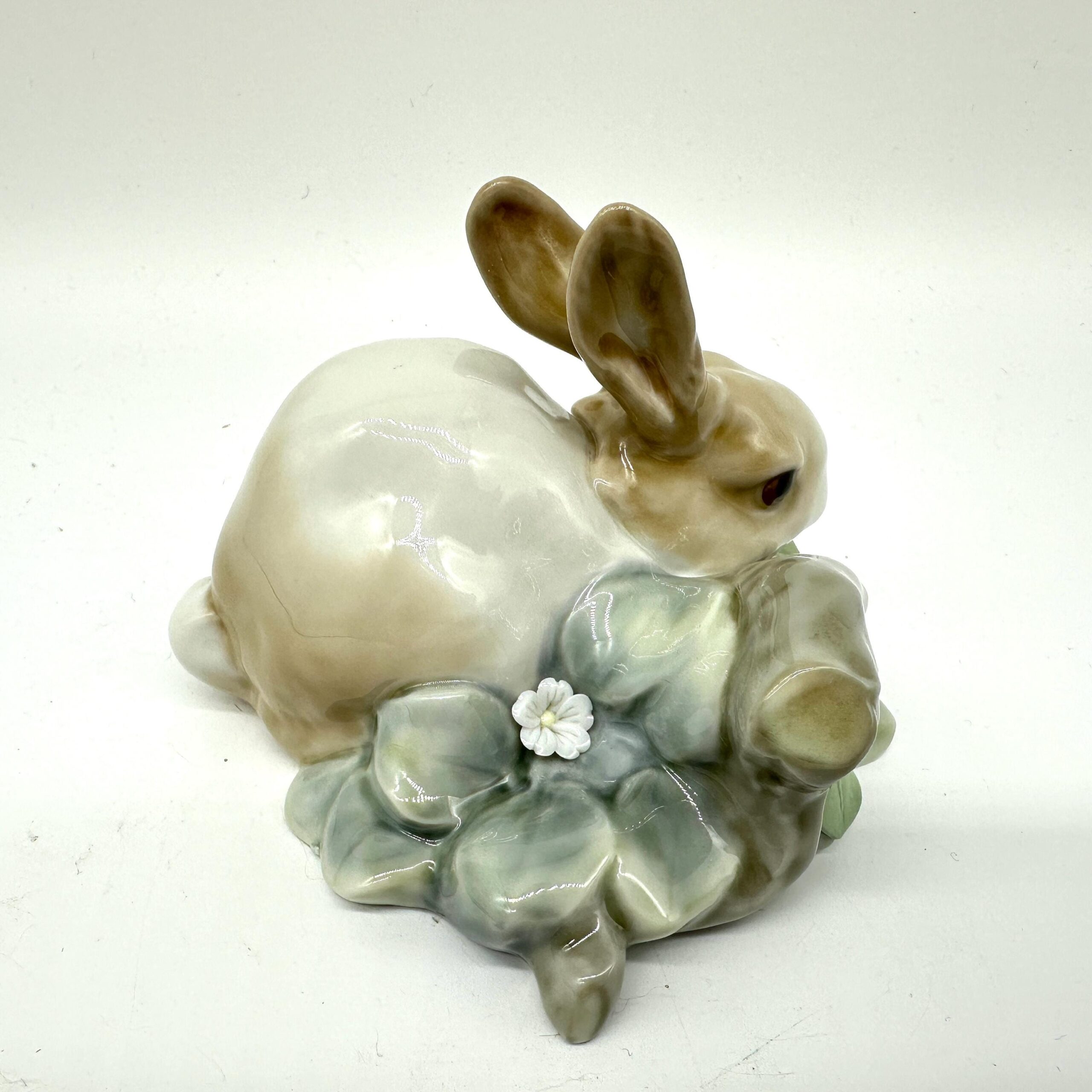 Lladro porcelain rabbit figurine photographed from low front angle showing brown facial features, cream body, and leafy botan