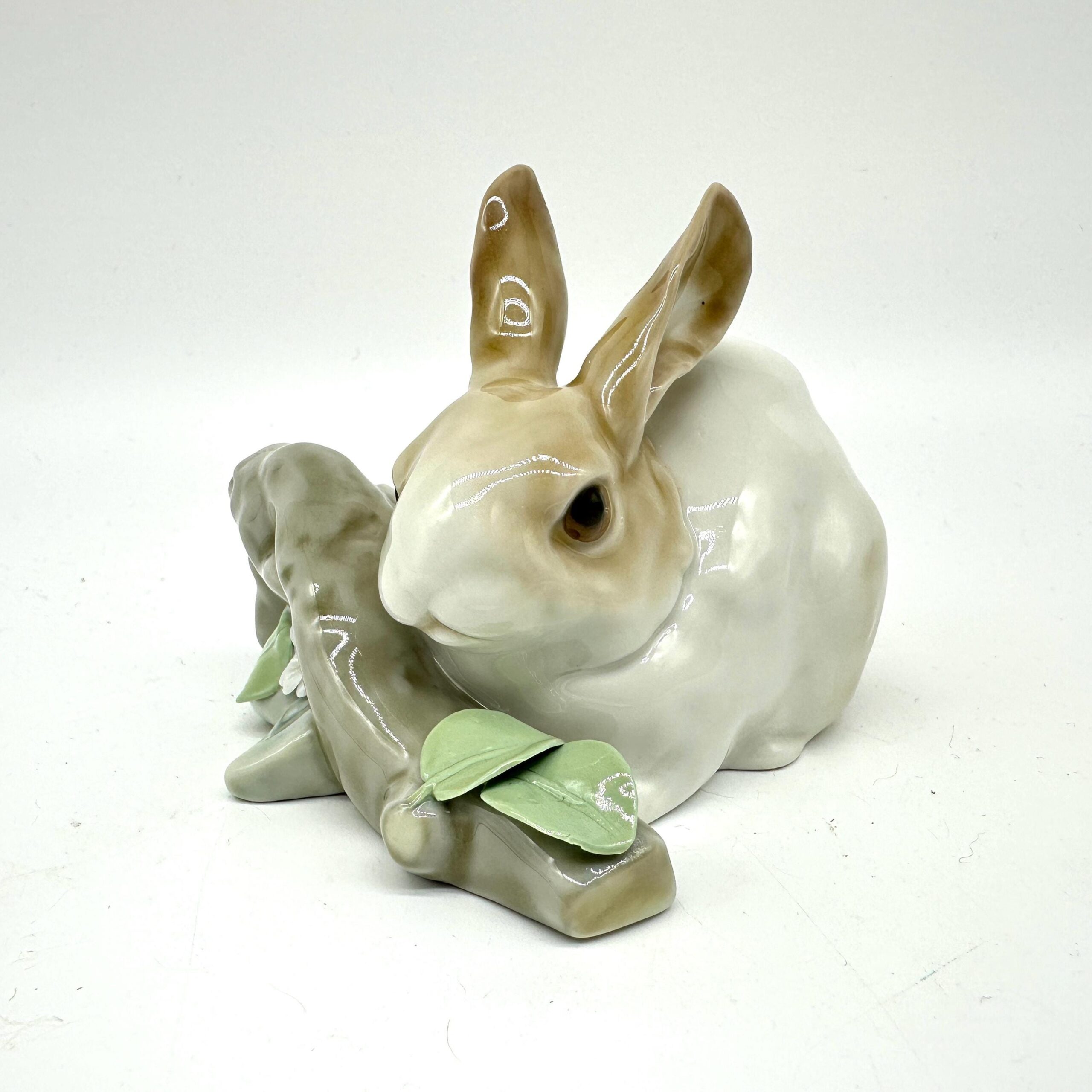 Lladro rabbit figurine photographed from elevated angle displaying upright ears, white glazed body, and scattered green leaf