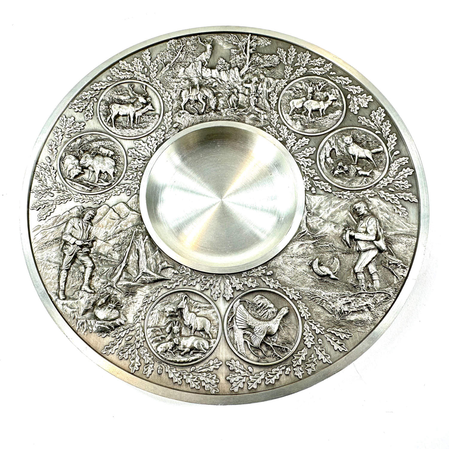 Overhead view of relief pewter plate showing twelve zodiac-style medallions and ornamental hunting motifs arranged around cen