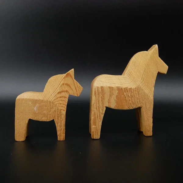 Pair of hand-carved wooden Dala horses in natural wood finish, larger horse with arched neck alongside smaller companion piec