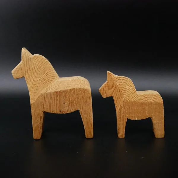 Pair of wooden Dala horses at rest position with smaller horse in foreground, showcasing overall set composition and relative