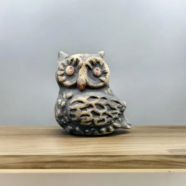 Quarter-view display of cream-colored ceramic owl on wooden shelf with soft lighting emphasizing texture and depth of hand-ca
