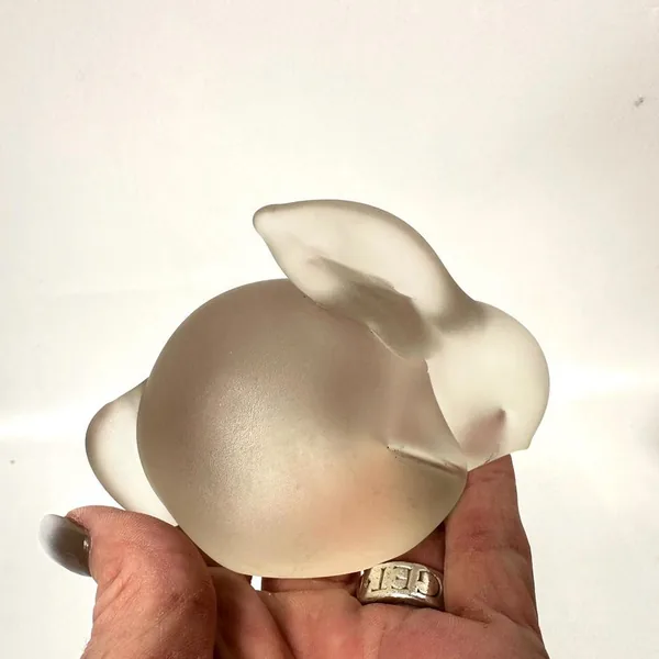 Rabbit sculpture in hand showing cream frosted glass back profile, smooth body curvature, and subtle ear articulation