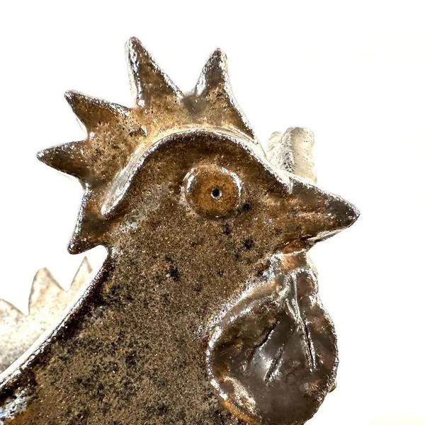 Rooster head close-up showing carved facial features, eye detail, beak profile, and textured glaze with warm brown metallic t