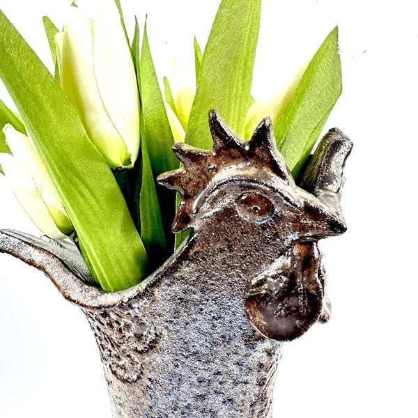 Rooster vase angled view displaying sculpted head profile, textured body surface, and fresh foliage emerging from the vessel