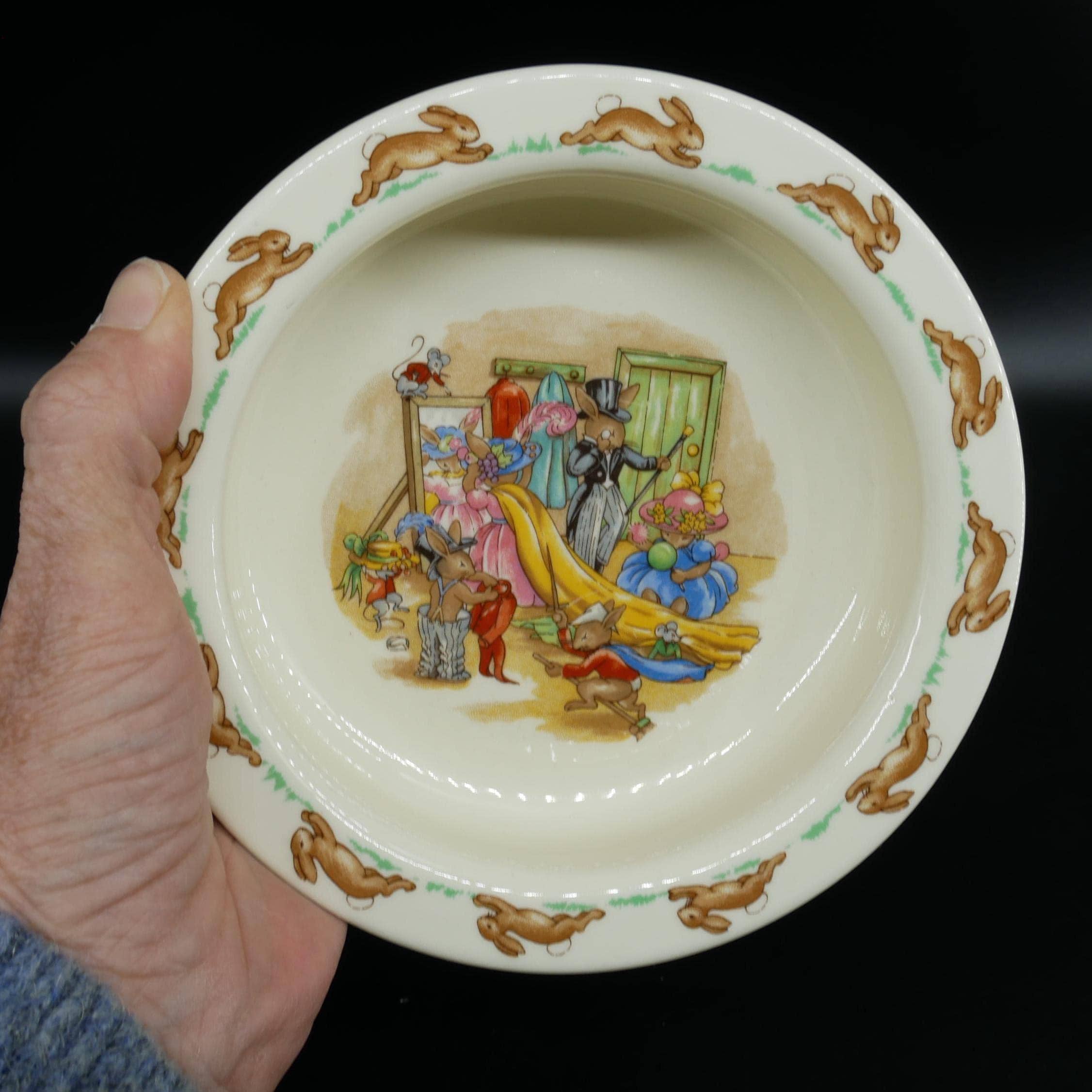 Royal Doulton Bunnykins fine bone china baby bowl held in hand, showing colorful dress-up scene with rabbits and mice, brown