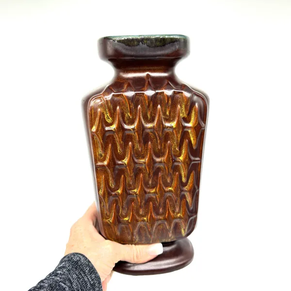 Scheurich pottery vase held in hands showing three-quarter view, brown satin glaze, deep zig-zag relief, cobalt rim visible