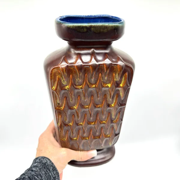 Scheurich vase in hands at eye level showing chevron texture detail, warm brown glaze tones, and blue interior rim opening