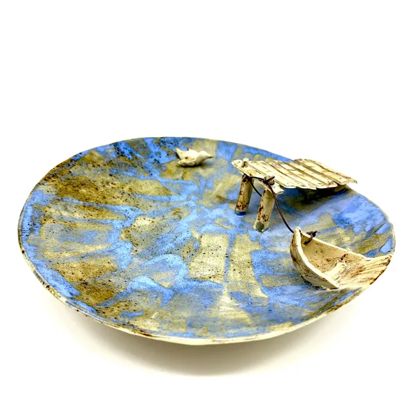 Side angle of pottery bowl emphasizing the dimensional rowboat and bird sculpture protruding from the blue and gold ceramic s