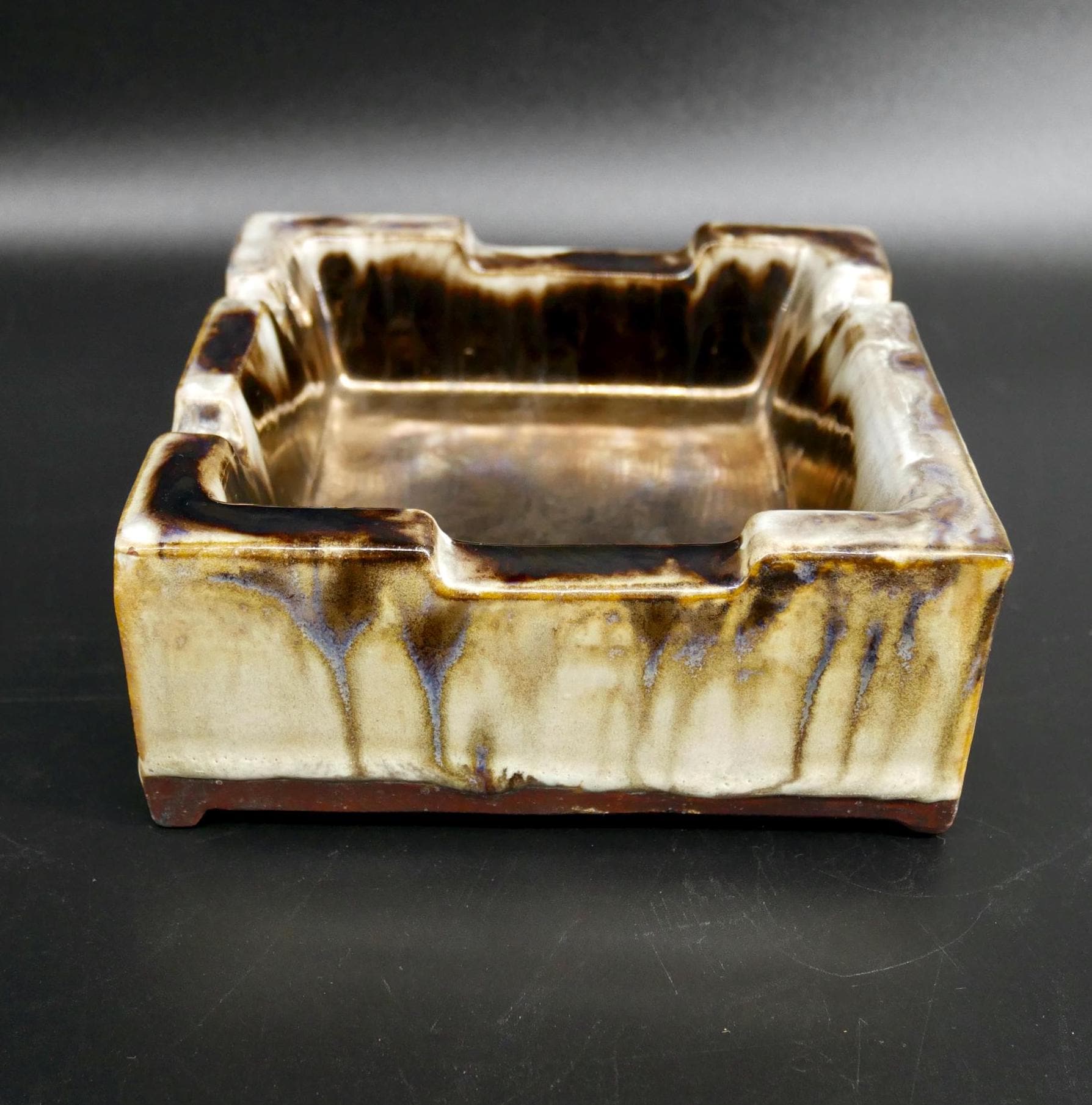 Square ceramic ashtray with molded walls, cream exterior with brown glaze drips, shallow interior bowl, side profile view