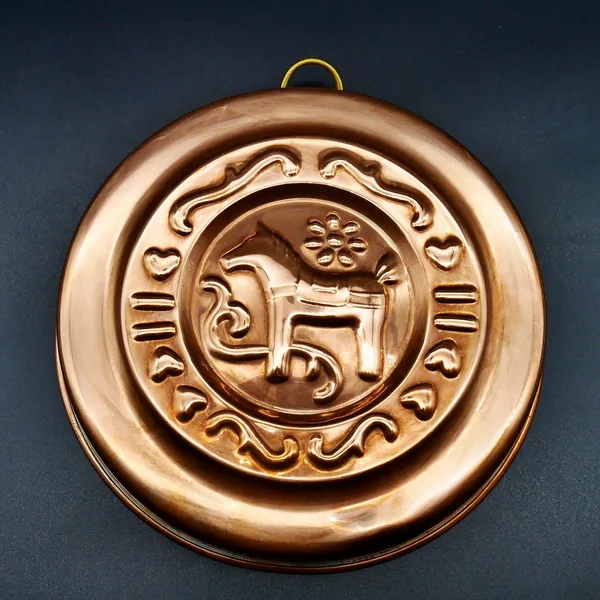 Straight-on view of copper mold with prominent brass hanging ring and symmetrical design