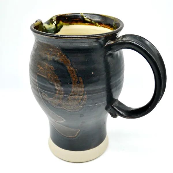 Studio pottery jug photographed from front with spout and handle visible, dark brown glaze with rustic surface texture visibl