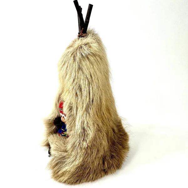 Three-quarter angle of reindeer skin teepee with visible wood frame structure and doll's traditional red hat protruding from