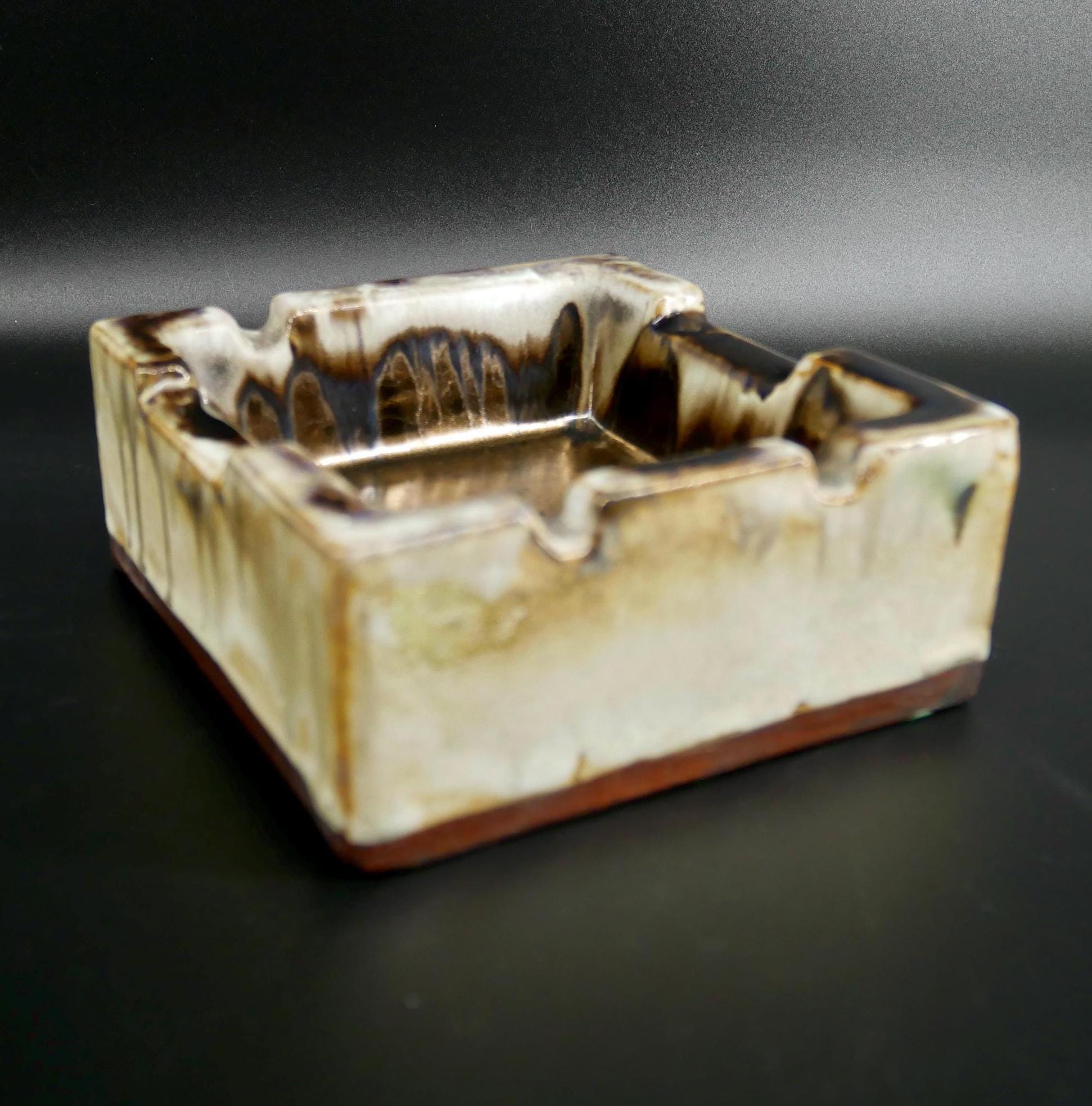 Three-quarter view of vintage ceramic ashtray, cream base with dripping brown glaze, rounded rolled rim edges, studio pottery