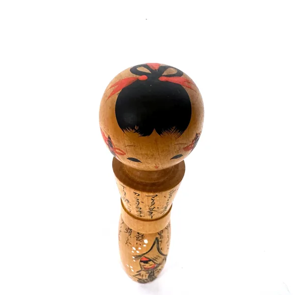 Top-down overhead view of kokeshi head with dramatic black-painted face and expressive red petal or petal-like motif
