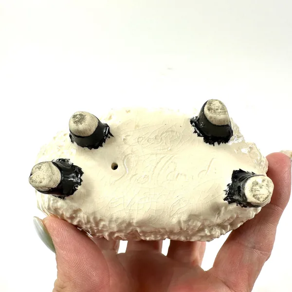 Underside of ceramic ram showing four black leg attachments and maker's base mark, palm-sized collectible pottery