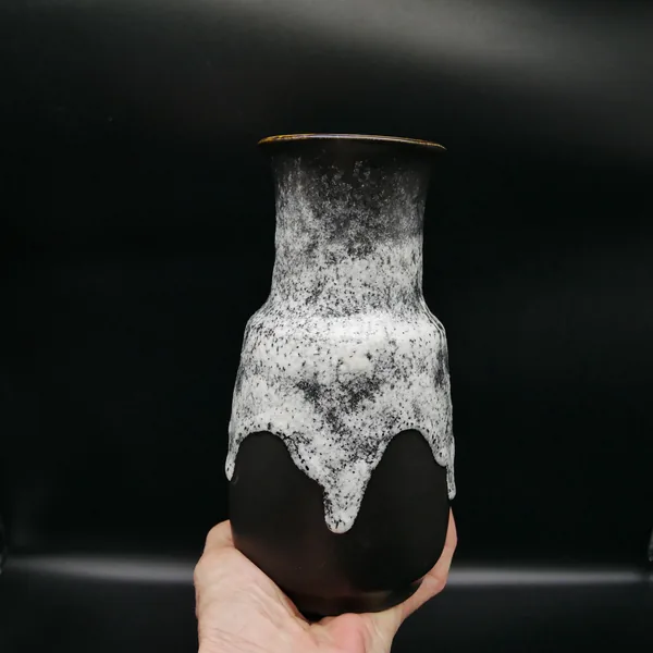 Vase held at angle showing full profile, white lava glaze with varied texture depth, black pedestal base support