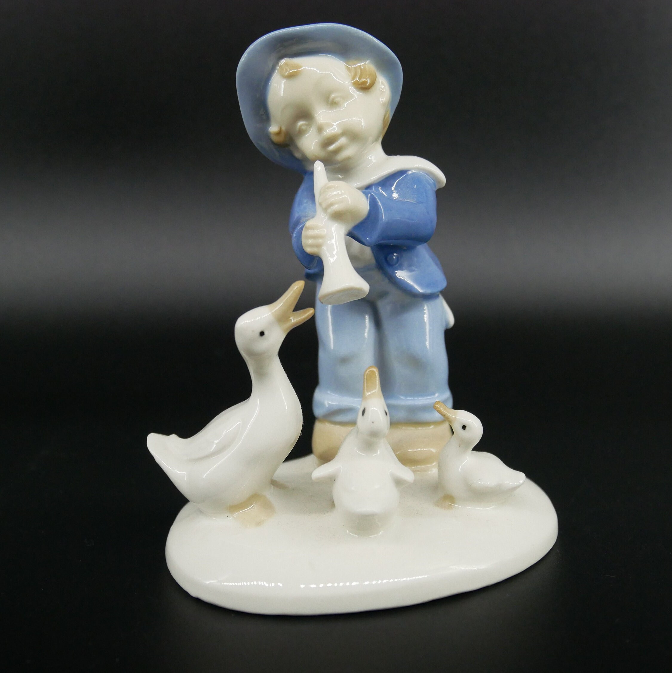 Vintage GDR porcelain boy figurine in blue outfit with three cream ducks on white base, front-facing view