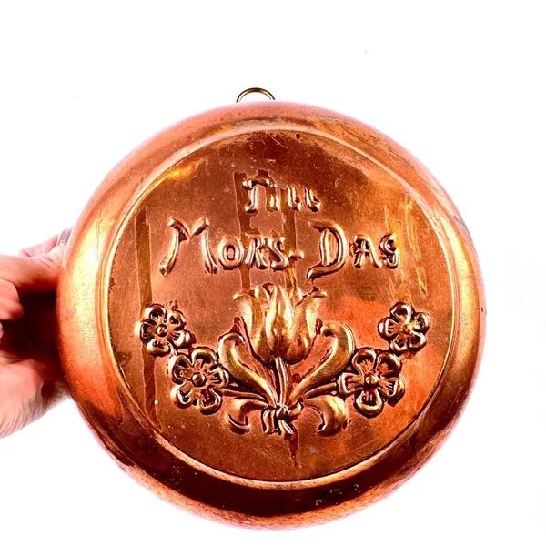 Vintage Scandinavian copper wall plate embossed 'Til Mor-Dag' with floral design, held in hand showing warm patina