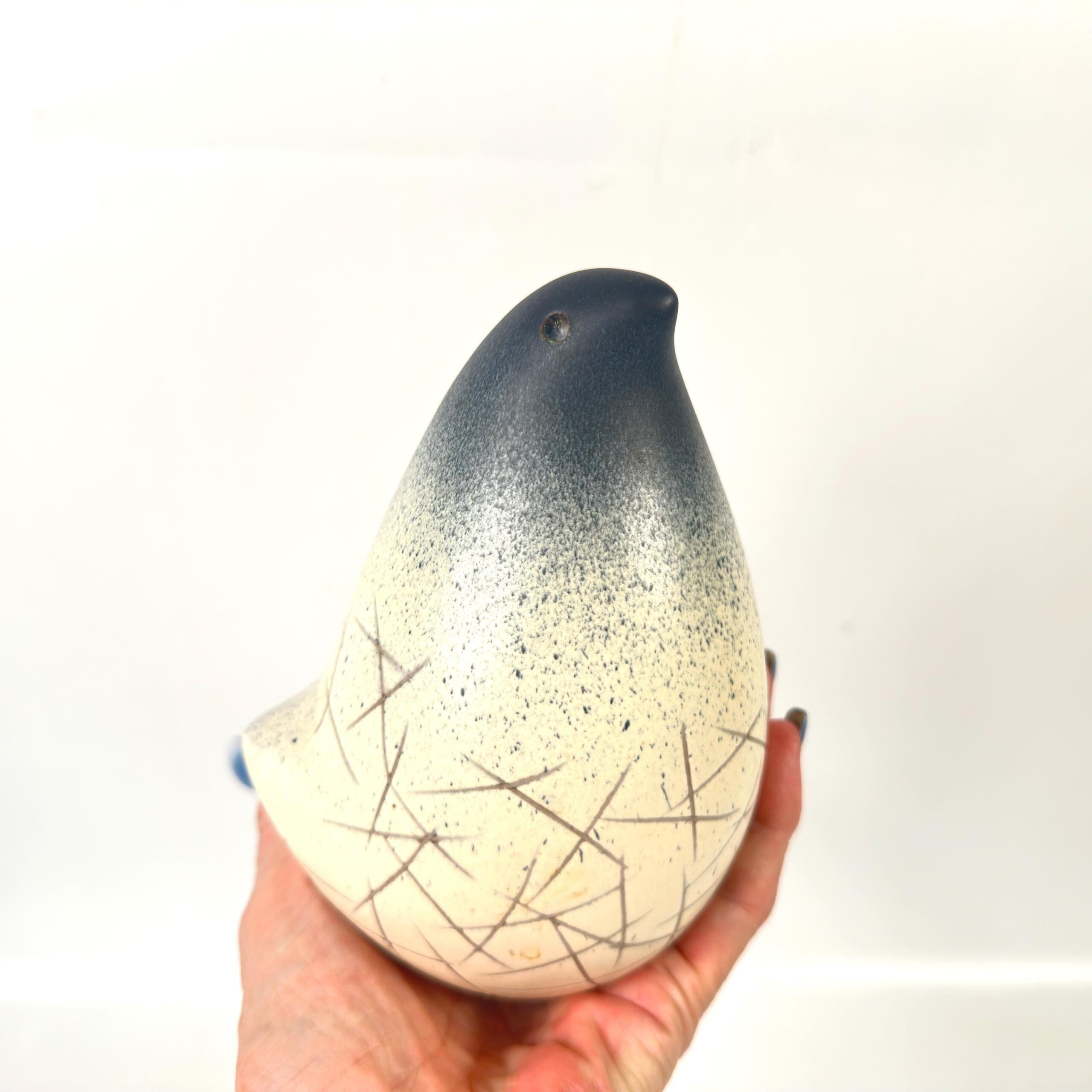Vintage Scandinavian studio pottery bird with charcoal speckled glaze and cream base, hand-carved linear details, held in pal