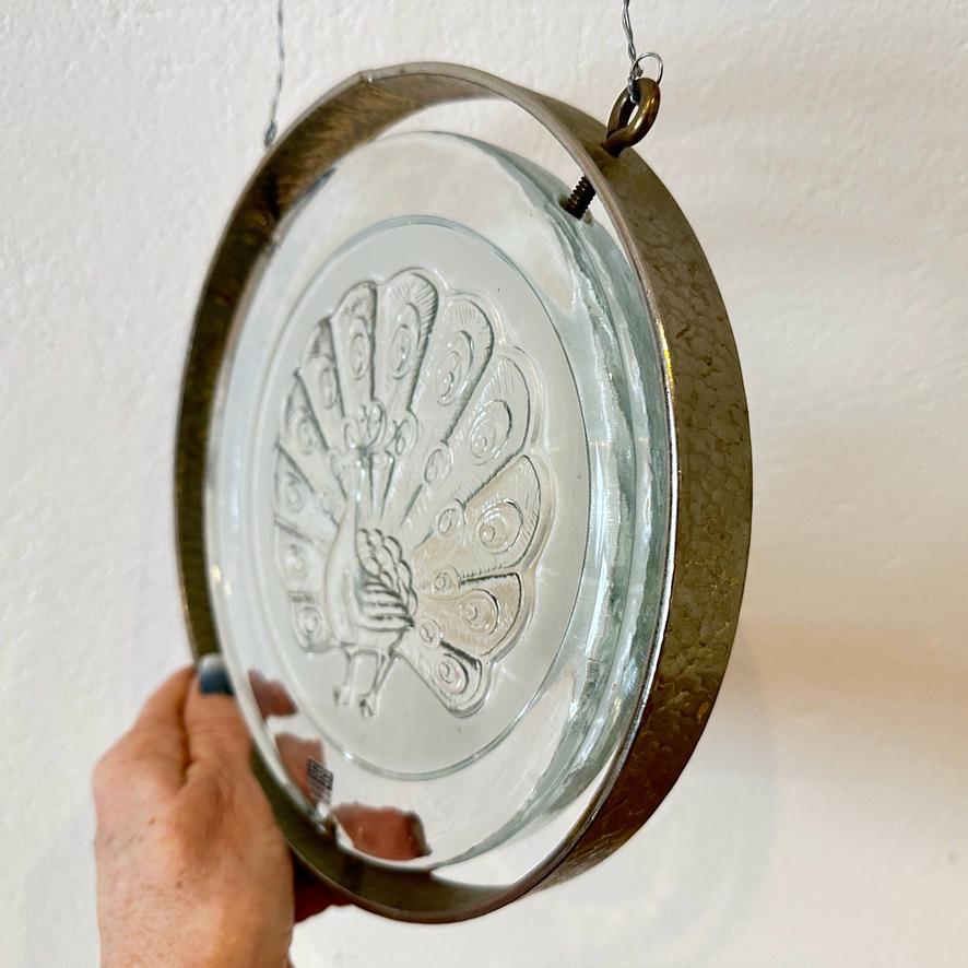 Wall plaque held at angle showing light transmission through pressed glass peacock design, peacock silhouette glowing
