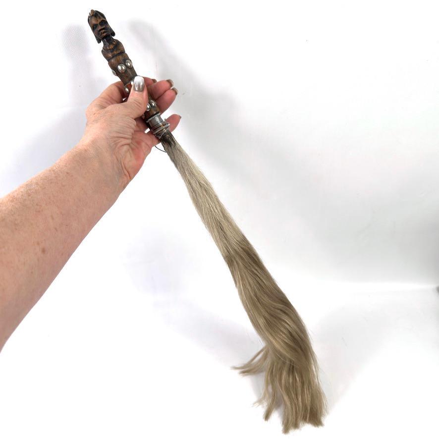 Angled hand grip showing carved wooden head sculpture from front angle, leather binding visible, horsehair sweeping below