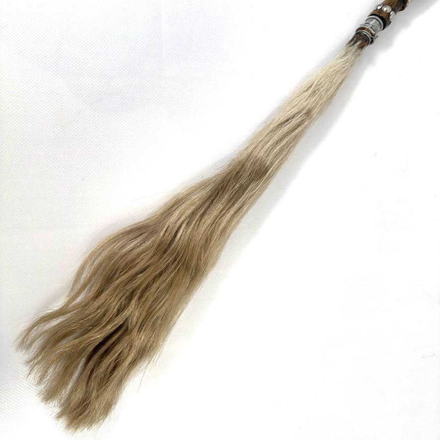 Angled side view of fly whisk revealing carved wooden handle details, metal inlay work, and full length horsehair bundle