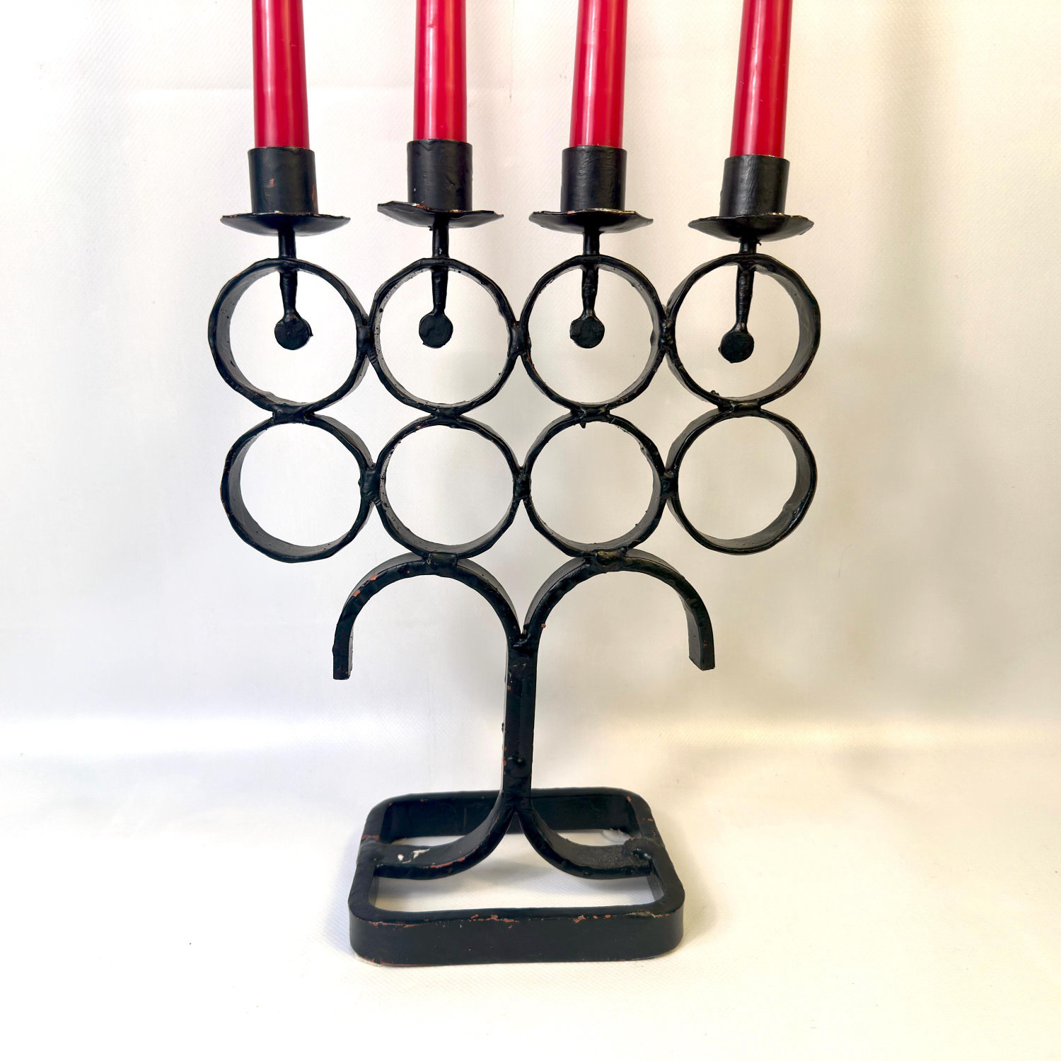 Angled view of iron candelabra showing stacked circular rings and four black candle cups with burgundy candles