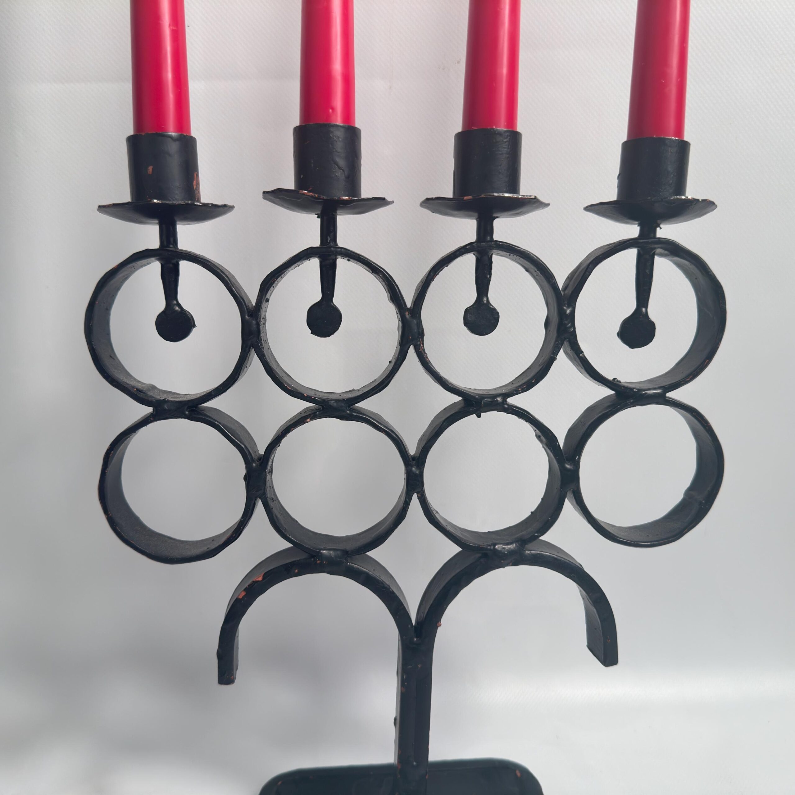 Close detail view of wrought iron rings and candle cup holders with burgundy taper candles, showing metalwork texture