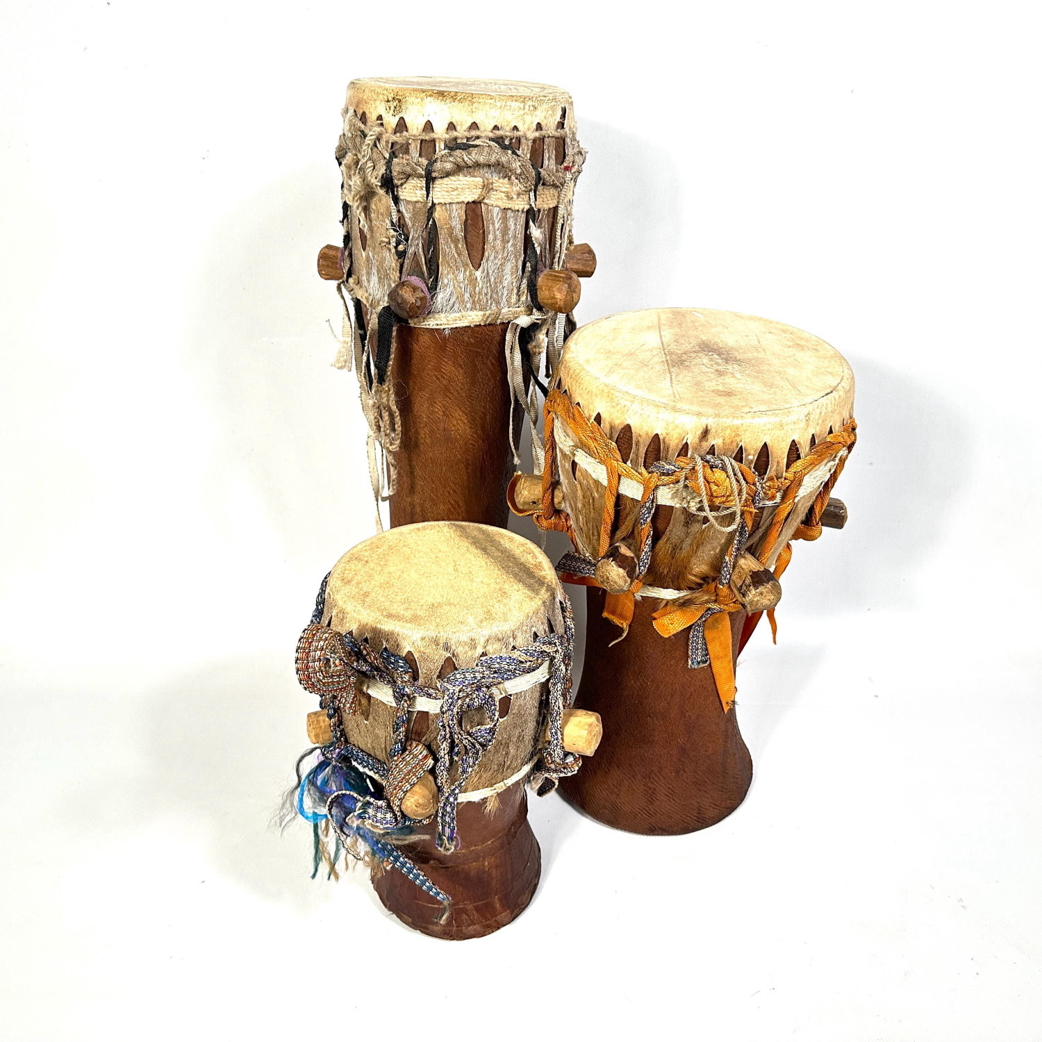 Collection of three African hand drums arranged in graduated formation showing all natural hide heads, carved wooden bodies,