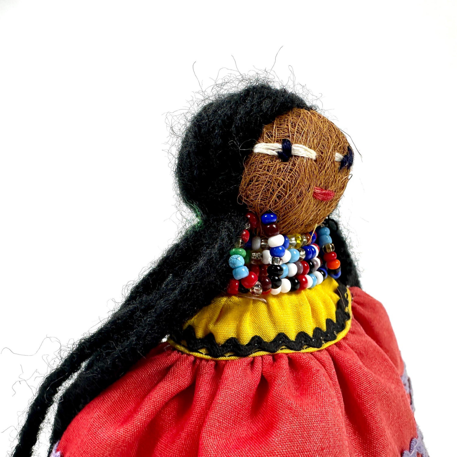 Doll head and shoulders in detail view highlighting black human hair, individual facial characteristics, and beaded adornment