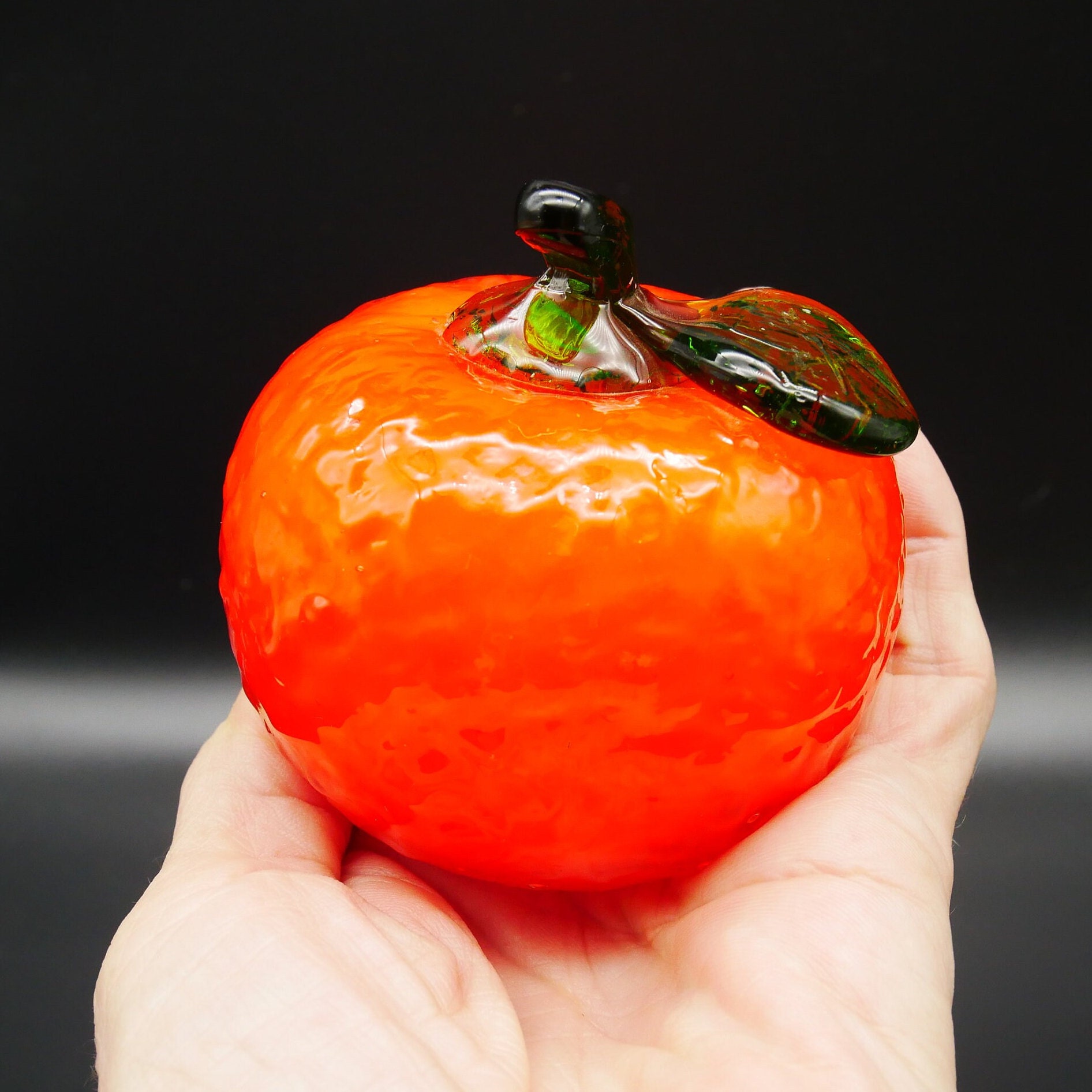 Glass fruit sculpture in hands showing textured surface and warm light passing through translucent orange glass