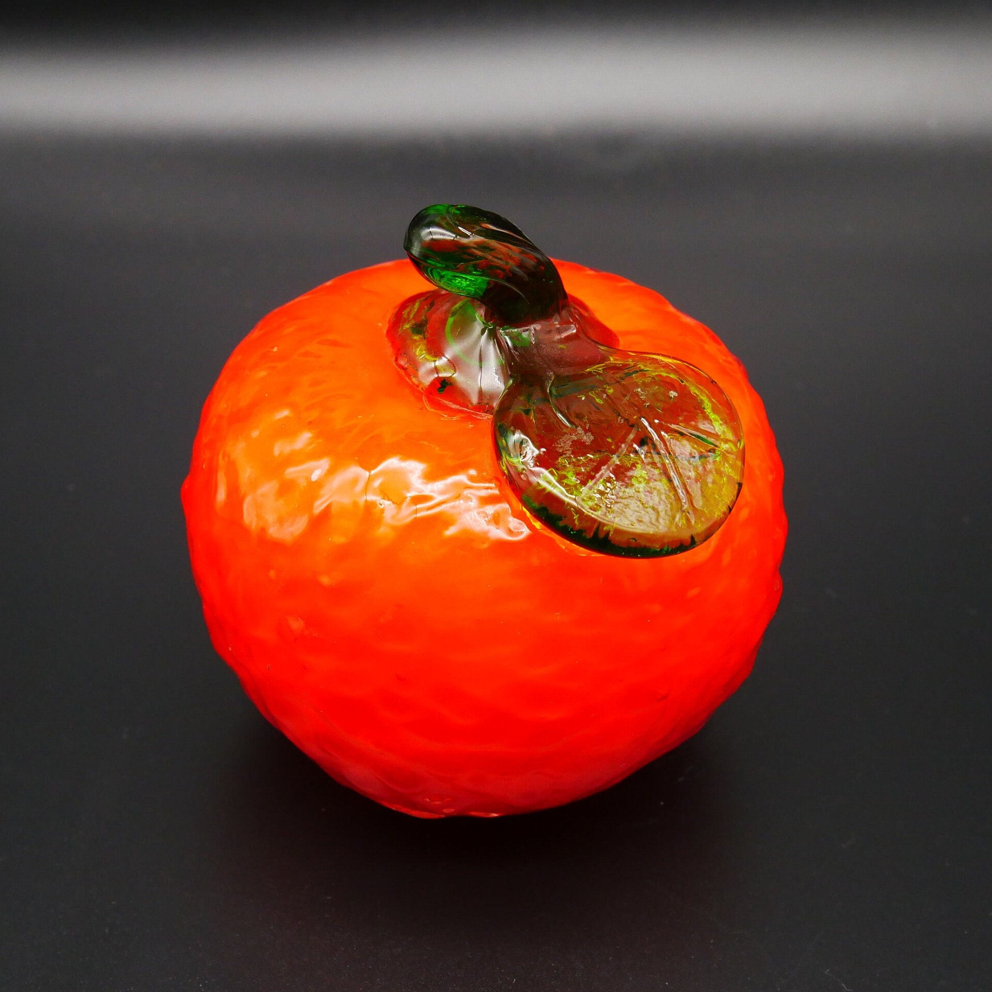 Glass orange sculpture tilted angle showing realistic bronze stem detail and warm orange saturation with light reflection