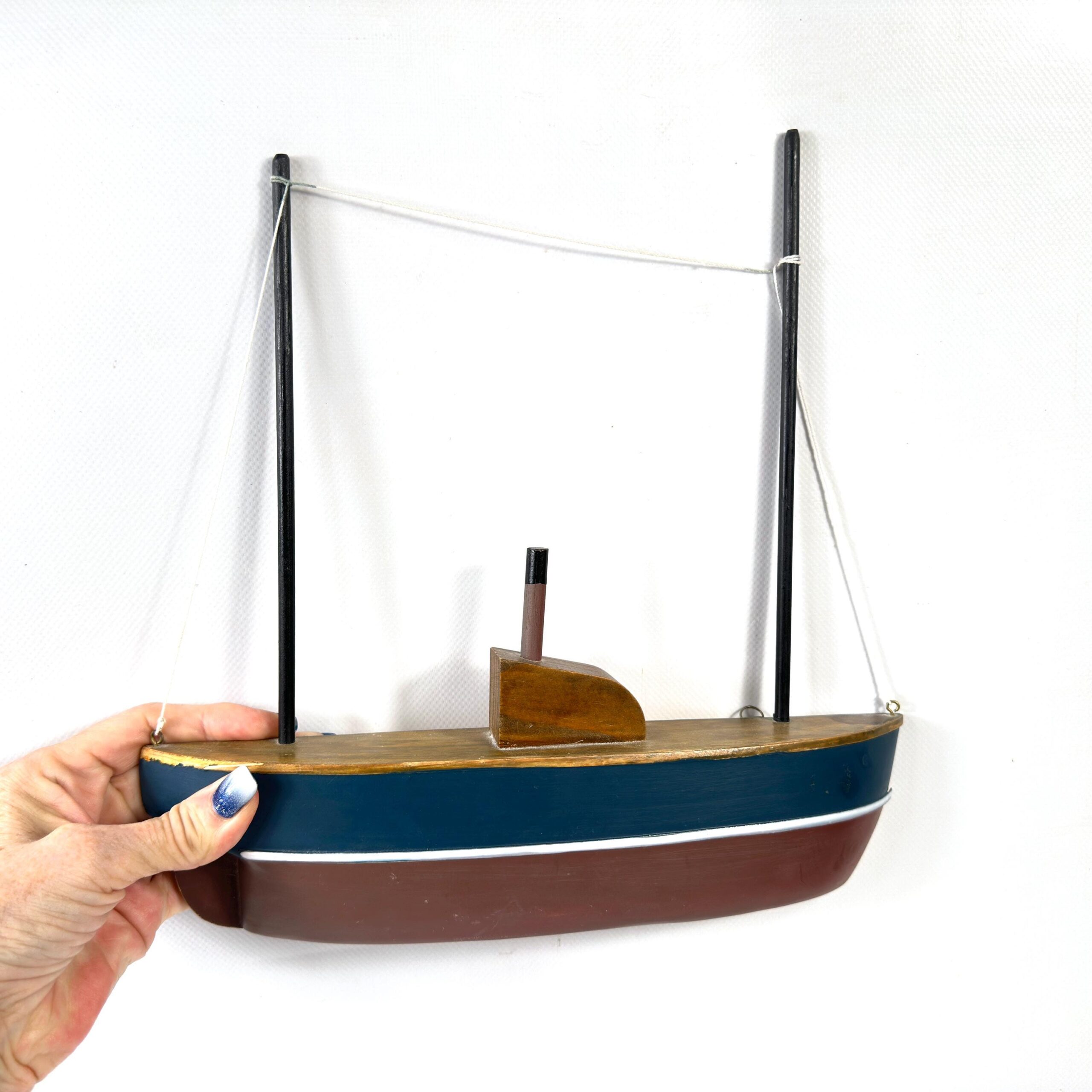 Half-hull wooden boat model in hand with fingers, warm natural wood tones, vintage patina, scale reference