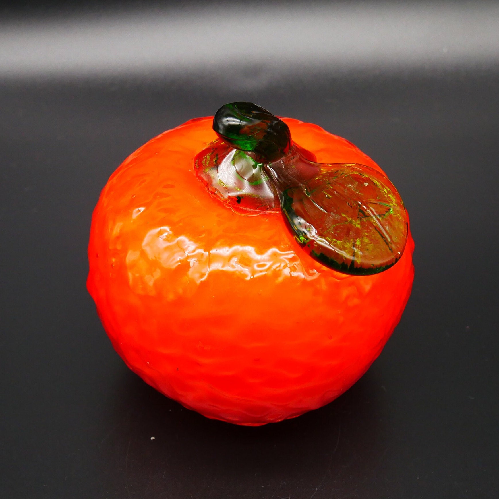 Hand-blown Swedish glass orange angled view revealing glossy finish, bronze stem details, and warm interior glow