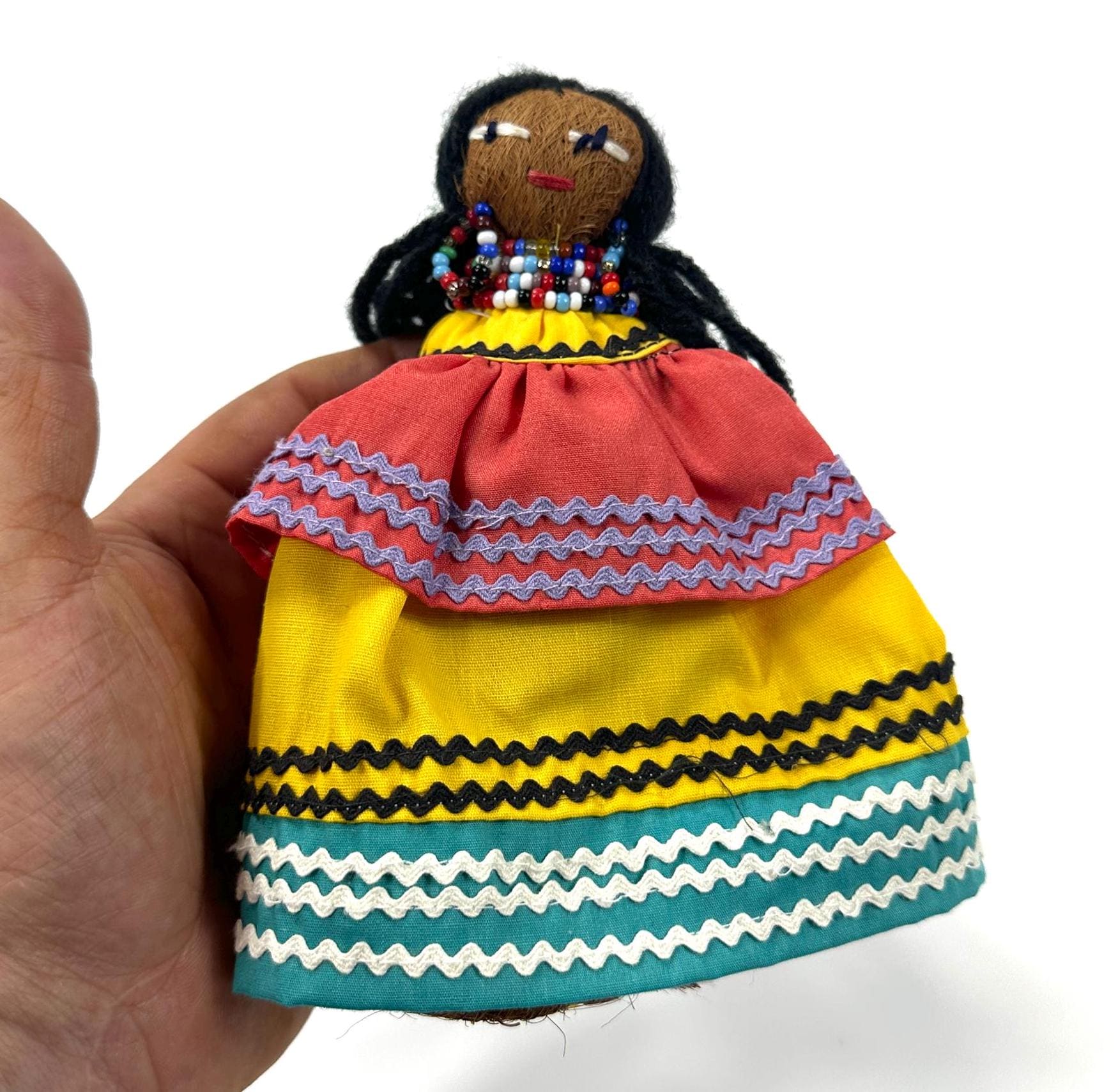 Hand-held doll in palm showing scale and weight, natural palmetto fiber texture, beaded elements, and complete form in close