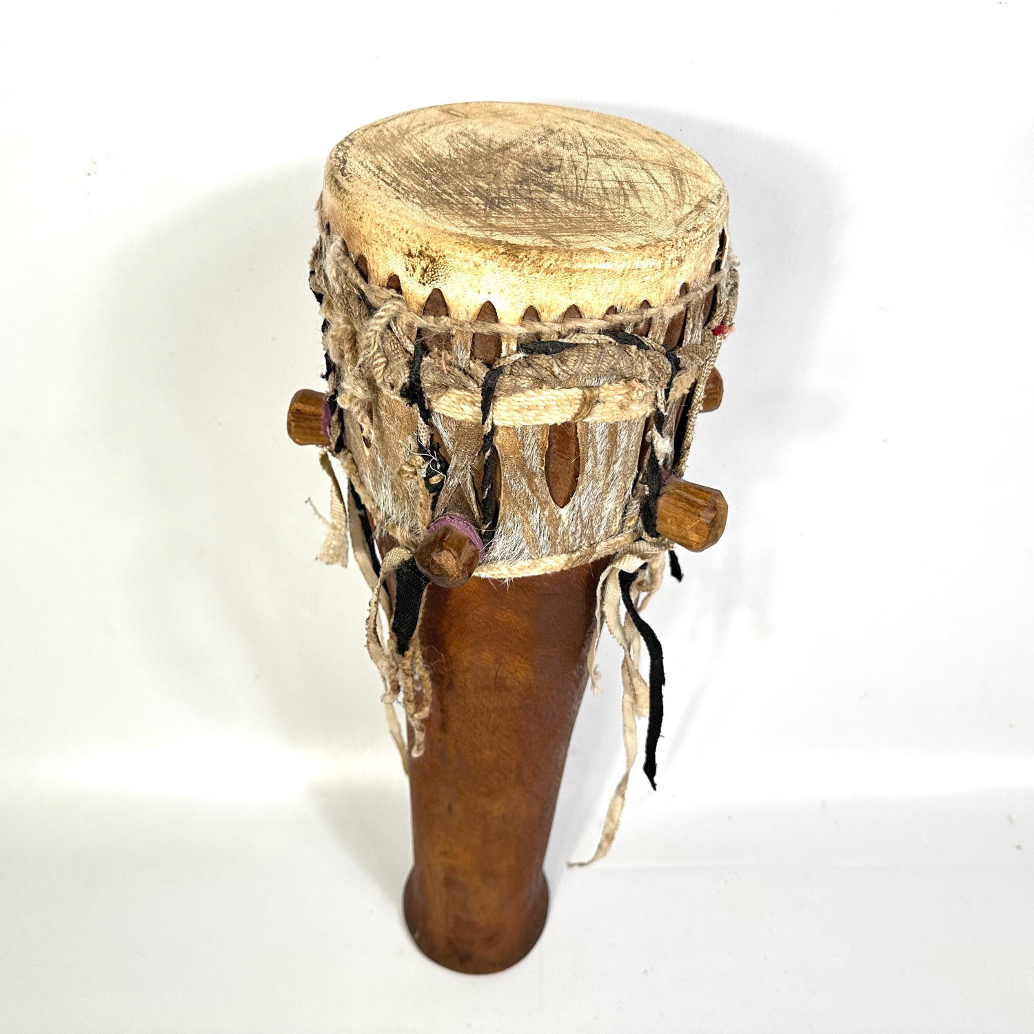 Large African hand drum displayed vertically showing carved wooden body, natural hide drumhead, and pendant rope details
