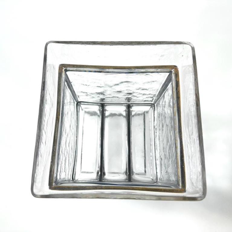 Looking down into glass cube showing interior walls' textured pattern, white candle holder centered below, and iron frame edg