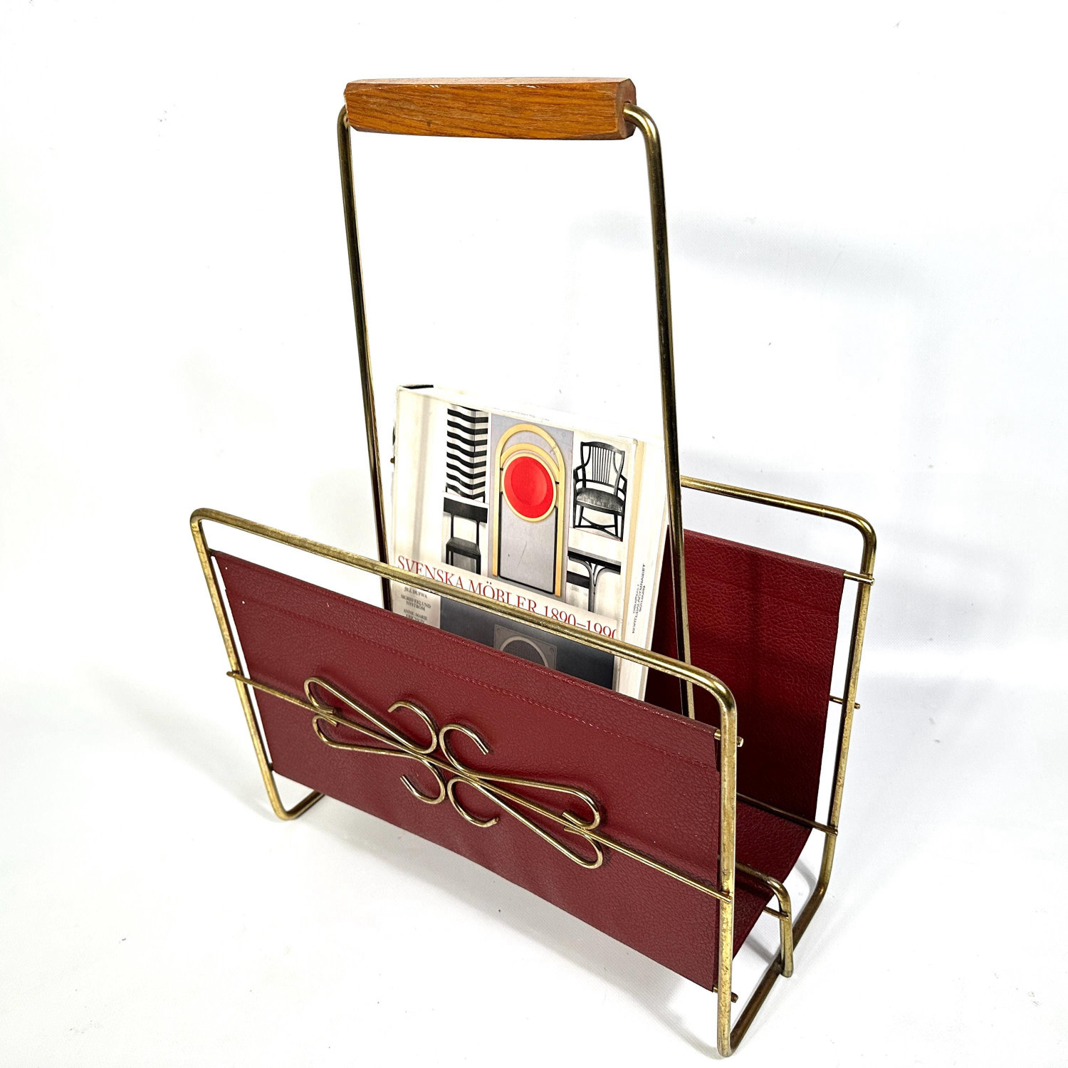 Mid-century magazine rack with brass frame, deep red faux leather panels, teak handle, and sculptural wire detail, front view
