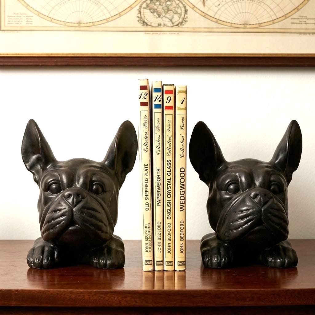 Pair of black moulded plastic bulldog bookends flanking vintage books on wooden shelf, classic mid-century desk decor