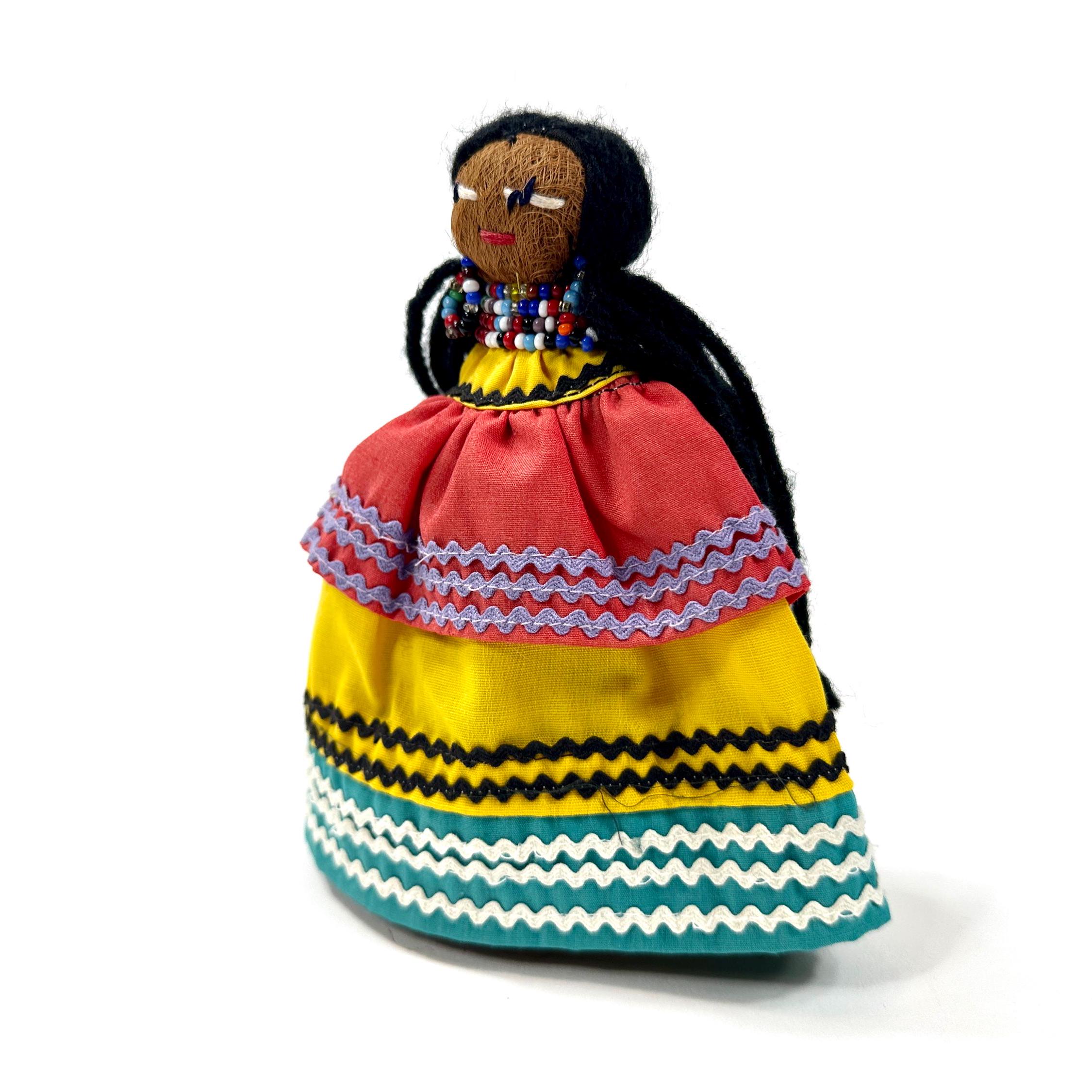 Seminole doll three-quarter angle revealing layered skirt construction with chevron and striped textile details in warm and c