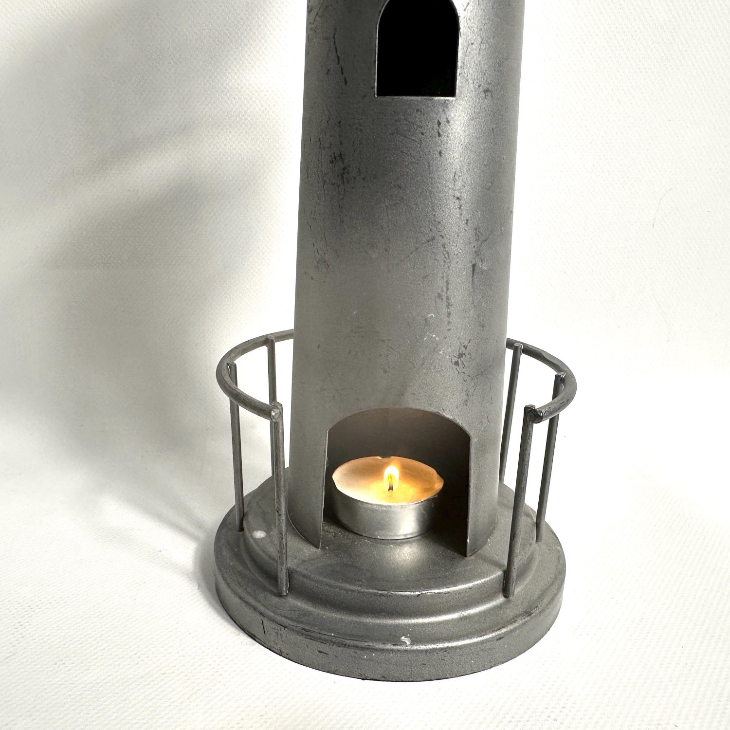 Side angle view of grey metal lighthouse with burning tealight in lower platform railing section