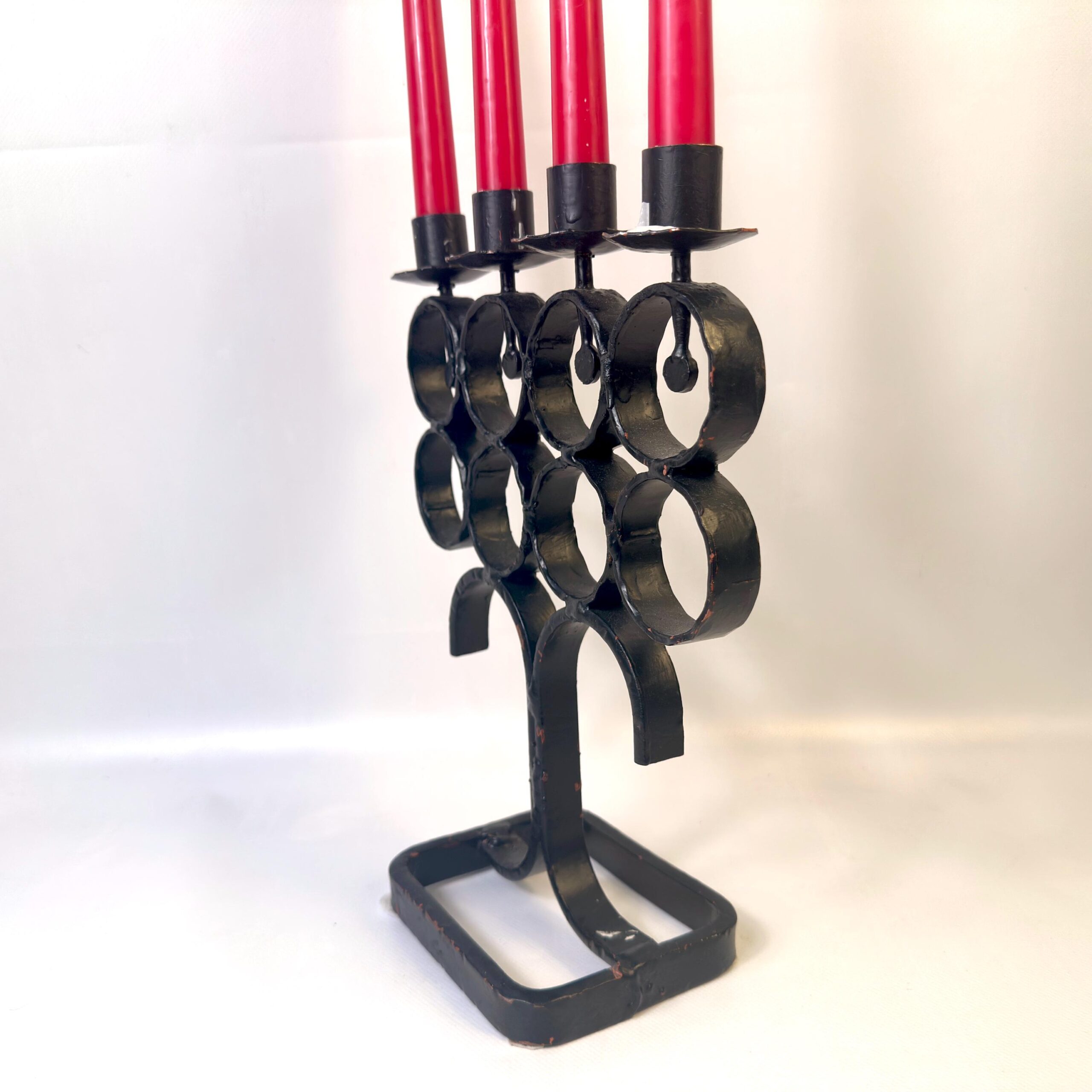 Side profile of iron candelabra showing curved legs, stacked rings, and four candles in profile arrangement