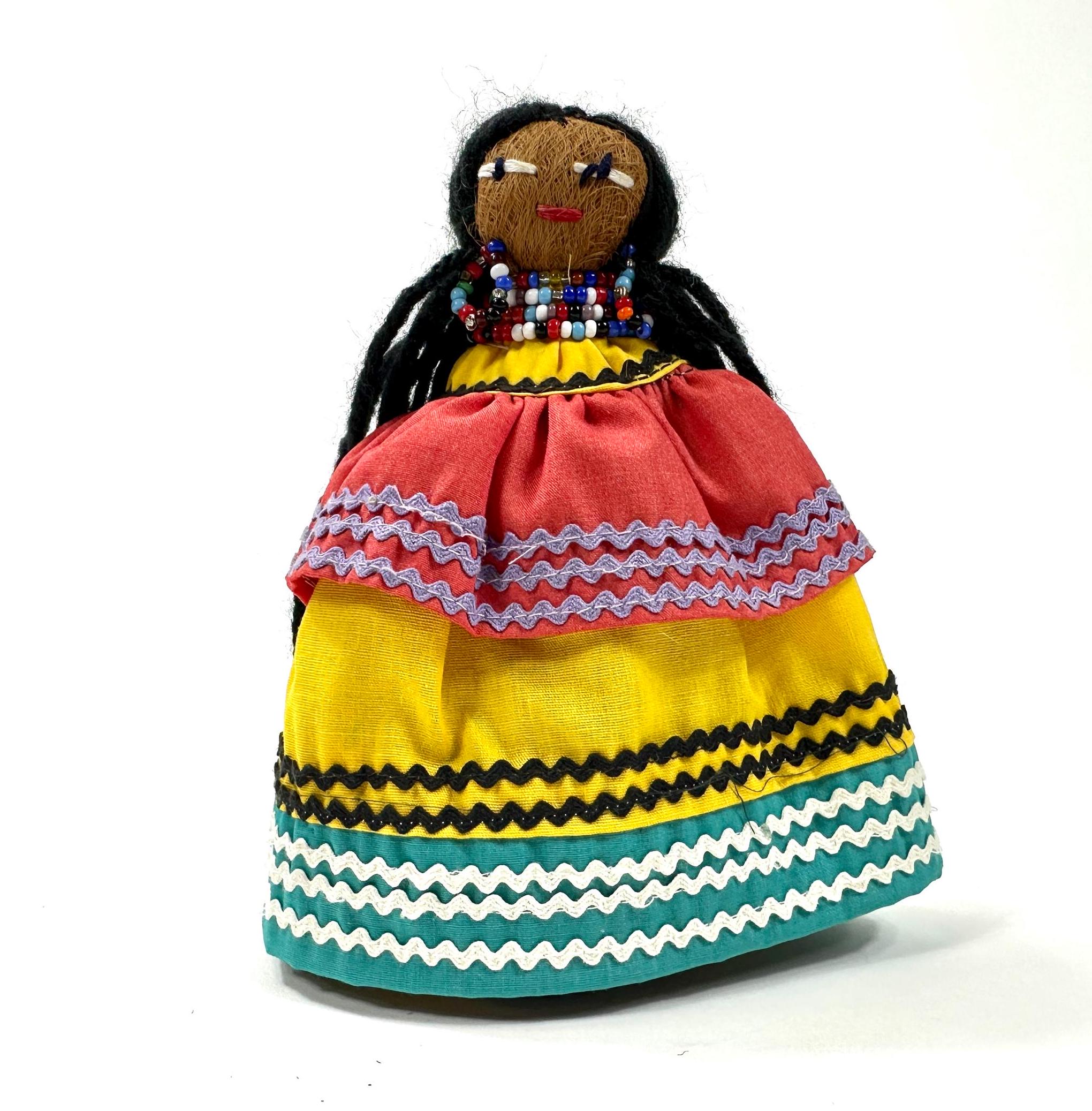 Straight-on view of complete doll figure with palmetto husk body, geometric patterned skirt in coral, gold, and teal striping