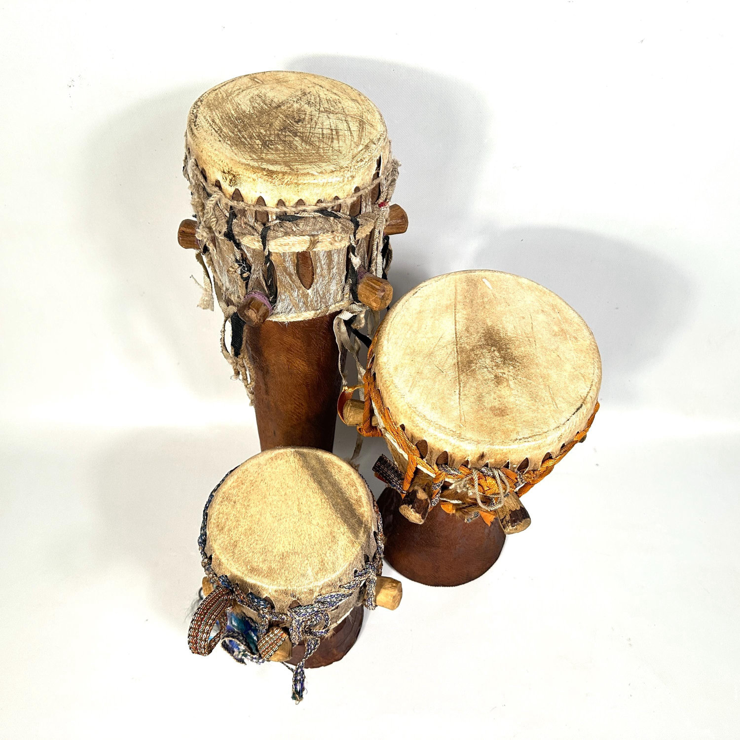 Three African hand drums arranged in triangular formation showing carved details, natural patina, and individual rope binding
